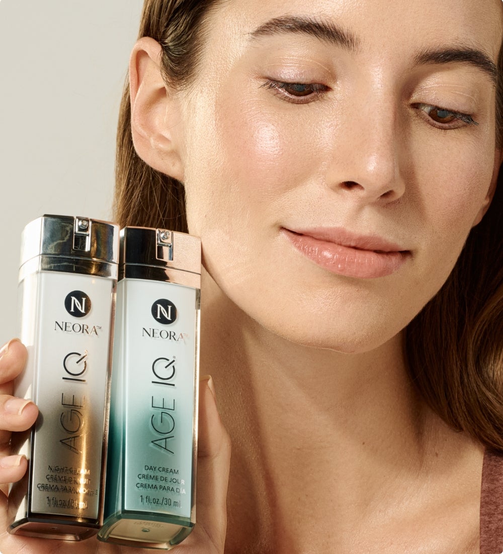 A man with face cream on his under-eye holds up a bottle of Age IQ Night Cream to his neck and shoulder.